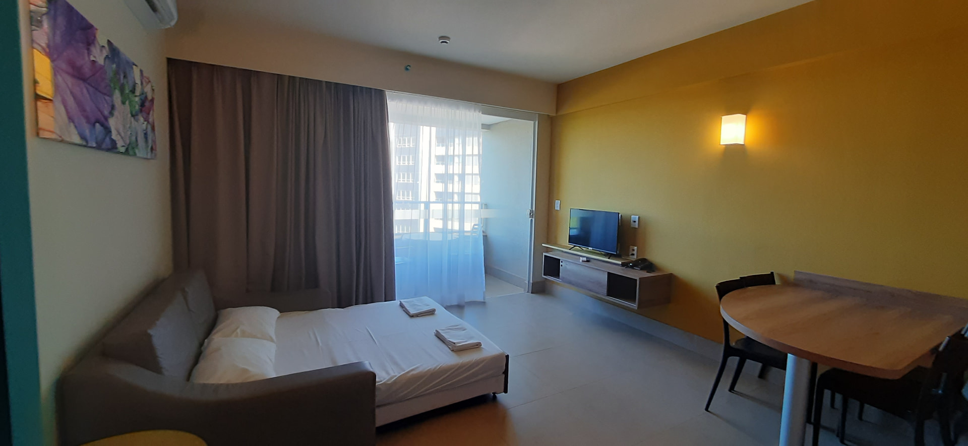 Sala com sofá-cama aberto, TV e mesa de refeições